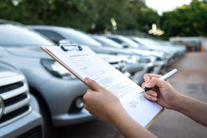 des mains tenant des papiers et des stylos devant plusieurs véhicules de société alignés