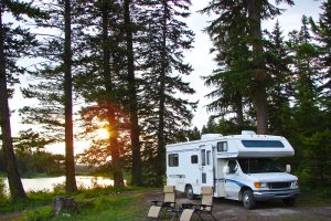 camping-car garé dans la forêt près de deux chaises d'extérieur