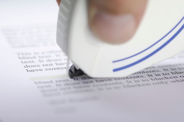 doigts tenant un rouleau correcteur blanc contre une feuille pour corriger un document