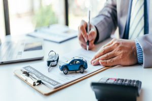 homme signant un contrat sur lequel une voiture miniature et une clé sont posées