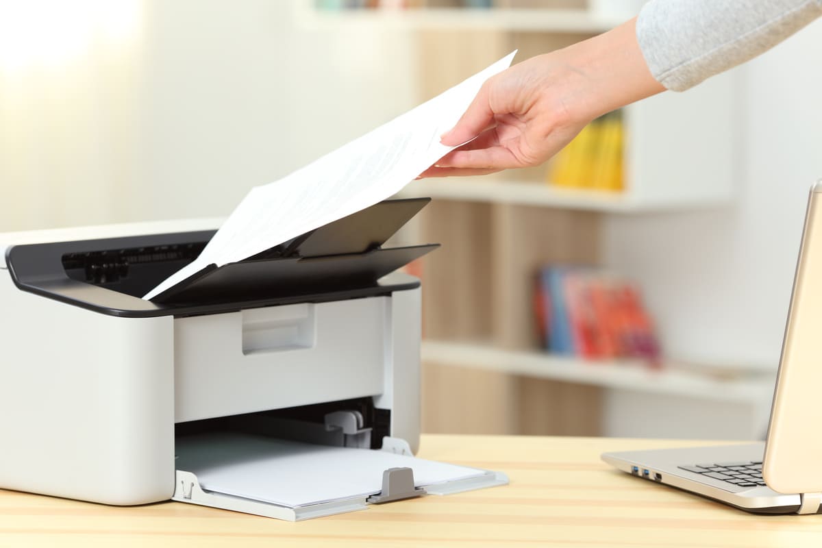 main prenant une feuille sur l'imprimante blanche placée sur la table près d'un ordinateur 
